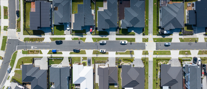 Aerial view of a suburban residential neighborhood with houses, streets, and parked cars.